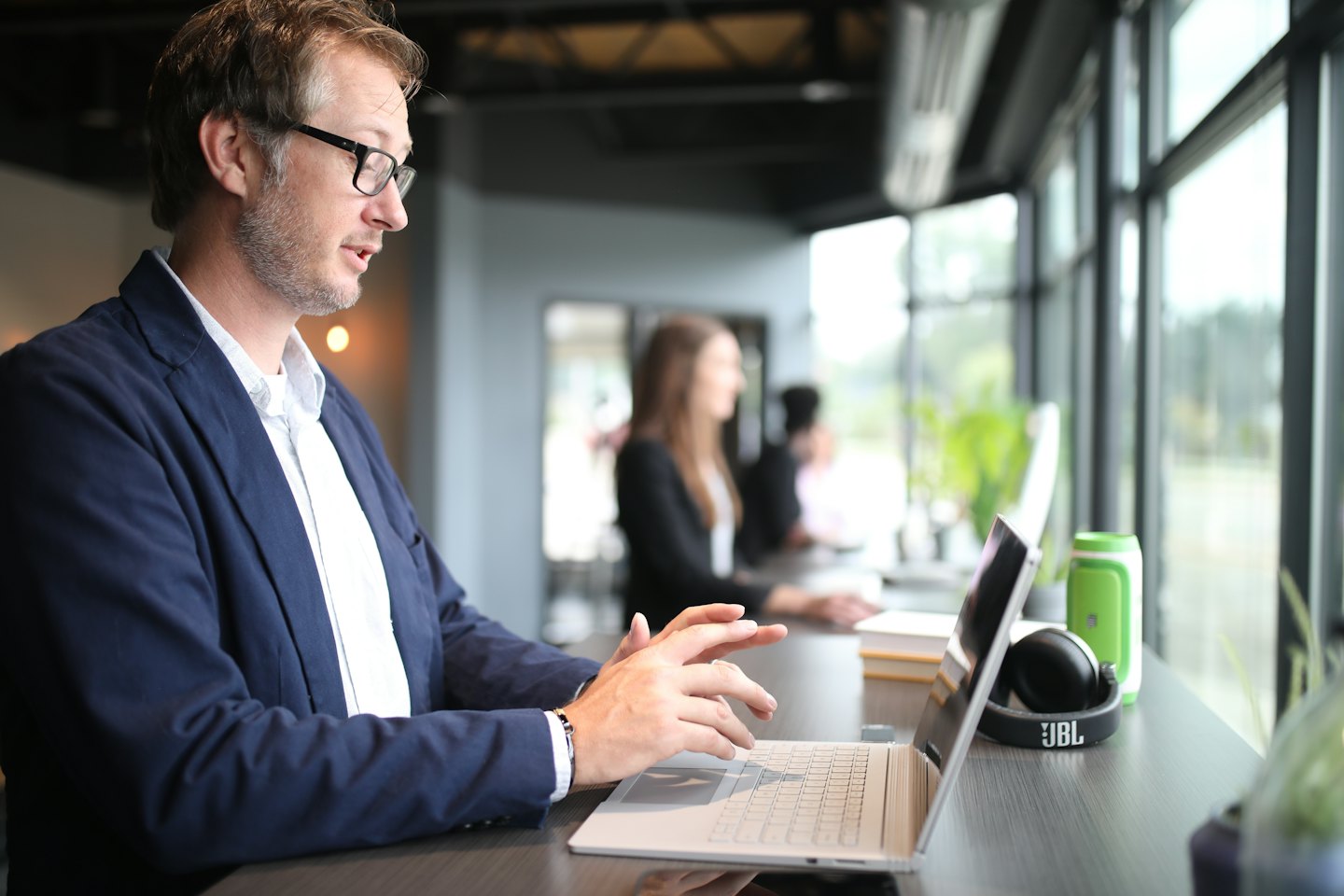 Man in glasses works on laptop at office counter.